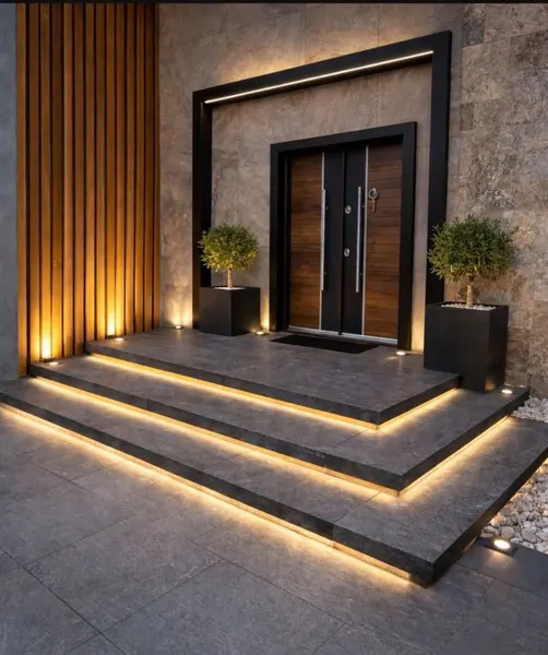 Front entry at dusk with lit stone steps, a black door frame, a wood slat wall panel and potted trees