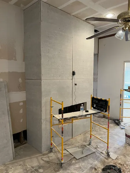 Fireplace wall covered floor to ceiling in cement backer board, with a rolling scaffold in front