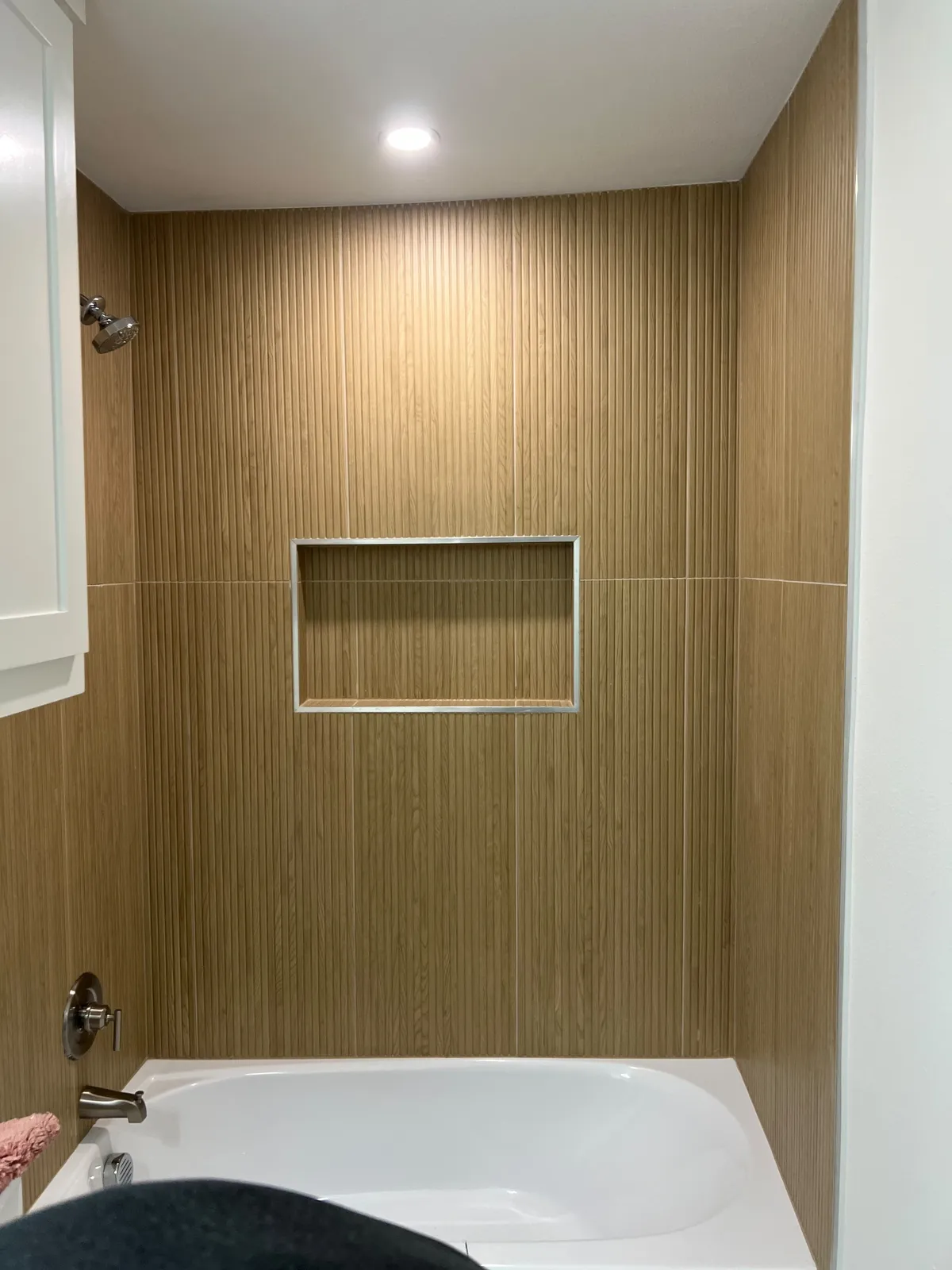 Tub surround in warm wood-look vertical tile with a metal-trimmed recessed niche above a white tub