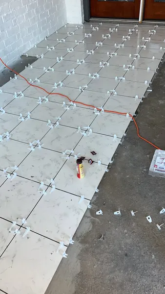 Large white marble-look floor tiles being set with leveling clips over a concrete slab