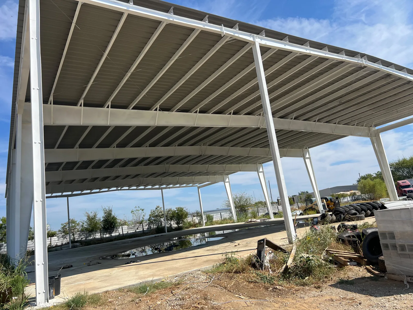Open-sided steel structure with white columns and beams under a metal roof on a commercial site