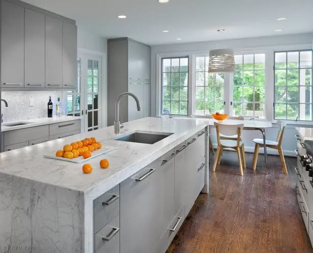 Bright kitchen with light gray cabinets, a white marble waterfall island with a sink, and a breakfast table by tall windows