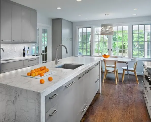 Bright kitchen with light gray cabinets, a white marble waterfall island with a sink, and a breakfast table by tall windows