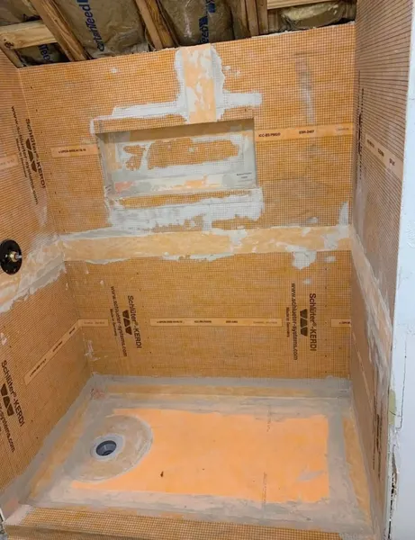 Shower under construction with orange waterproofing membrane on the walls, a framed recessed niche and a sloped floor around the drain