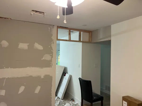 New wall with drywall taped and mudded, and open framing above the doorway beside it