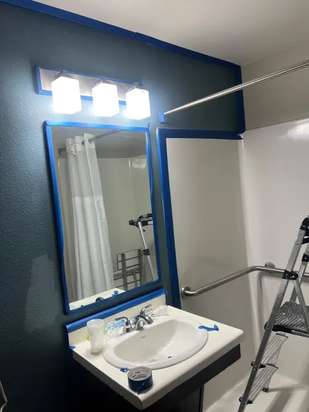 Bathroom mid-paint, with blue tape around the mirror, vanity and shower surround and a dark accent wall going on