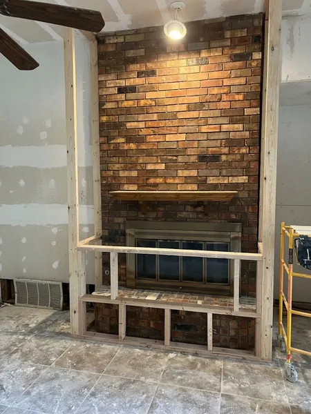 New wood framing around a brick fireplace, forming the base and sides of a larger surround