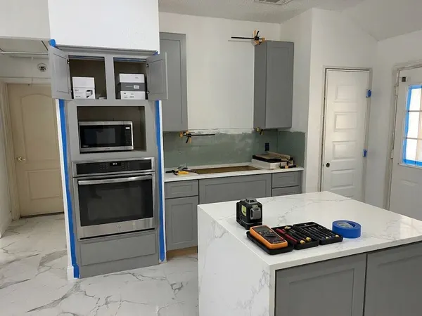 Tall gray cabinet with a wall oven and microwave, edges taped, and a sage glass backsplash going in behind the counter