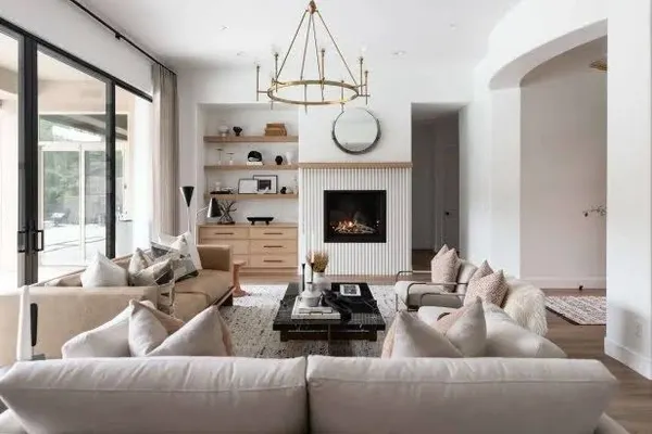 Bright living room with a fluted white fireplace surround, open wood shelving, a brass chandelier and cream sofas