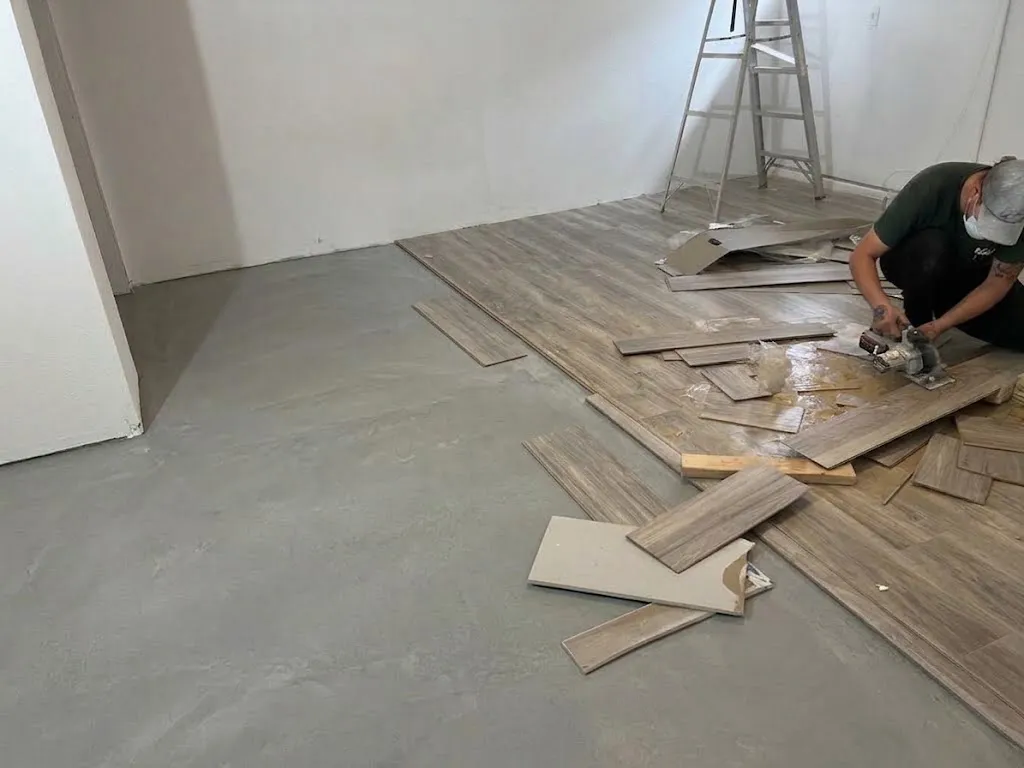 Installer cutting gray wood-look planks in an empty room, with part of the concrete slab still bare
