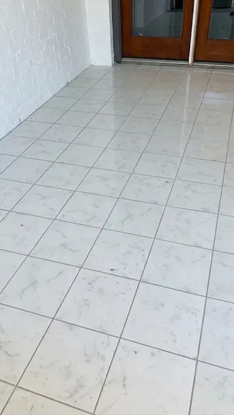 Finished white marble-look tile floor beside a painted brick wall and wood-and-glass doors