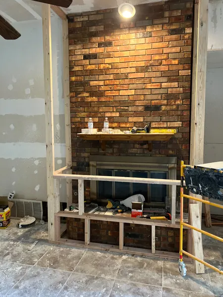 Old brick fireplace with a wood mantel and new wood framing being built around it