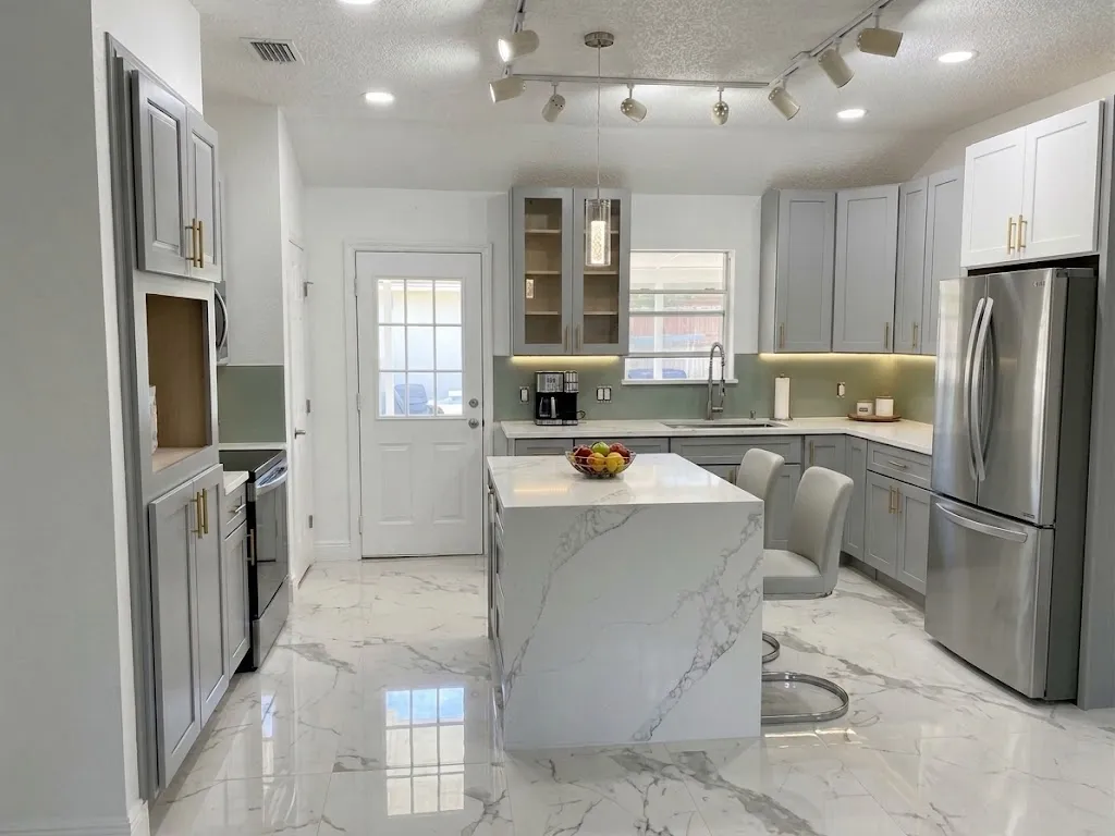 Finished kitchen with gray shaker cabinets, brass-tone pulls, a white waterfall island, a sage glass backsplash and under-cabinet lighting