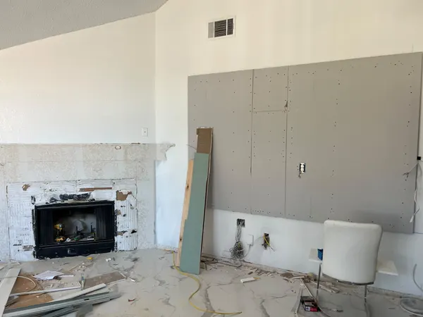 Fireplace with its painted brick surround partly removed and new gray board installed on the wall beside it