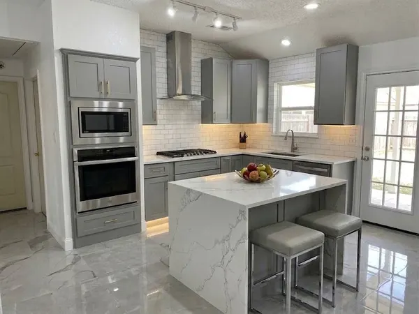 Gray shaker kitchen with white subway tile to the ceiling, a stainless range hood, a waterfall island and two gray stools