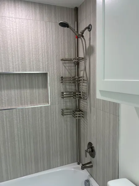 Tub surround in textured gray vertical tile with a metal-trimmed recessed niche and a handheld shower on a slide bar
