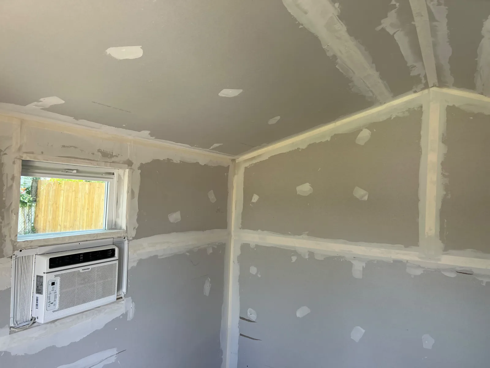 Shed interior with drywall taped and mudded on the walls and ceiling, and an air conditioner in the window
