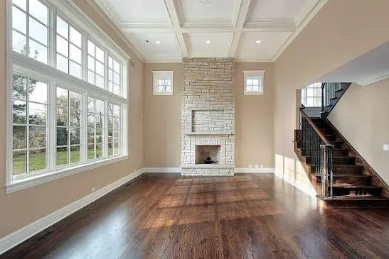 Empty living room with dark hardwood floors, a stacked-stone fireplace, a coffered ceiling and a wood staircase