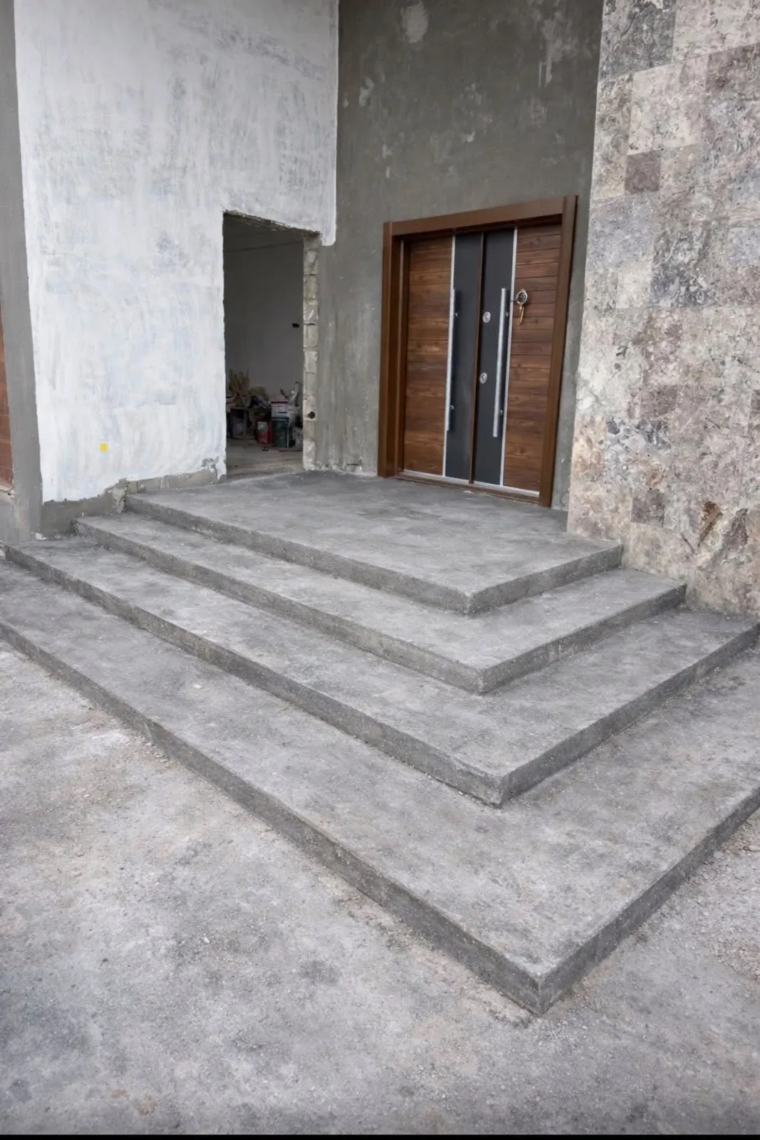 Wide three-tier concrete steps leading to a wood-and-black double front door beside stone wall cladding
